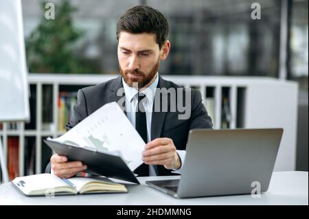 Smart confident caucasian bearded businessperson, ceo of company, top manager, financial expert, sits in modern office, concentrated studies financial documents, plans a development business strategy Stock Photo