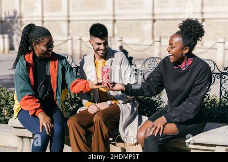 Three friends exchanging presents while sitting on a bench on a square Stock Photo