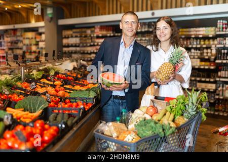 Portrait of a happy couple in a supermarket, holding a watermelon and pineapple in their hands Stock Photo