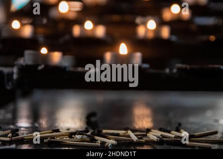 A closeup of burnt matches on the ground with a blurry background of burning candles in a Catholic church Stock Photo