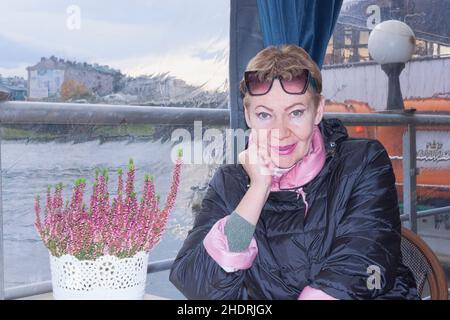 A portrait of a mature woman at a table in a cafe on the quay of the Vistula River in Krakow. The beginning of November Stock Photo
