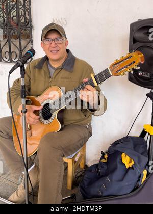 Cuenca, Ecuador, Dec 10, 2021 - man plays guitar as street musician for passing tips. Stock Photo