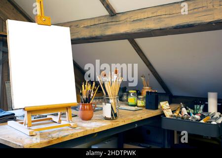 Artistic equipment in a artist studio: empty artist canvas on wooden easel and paint brushes Retro toned photo copy space Stock Photo