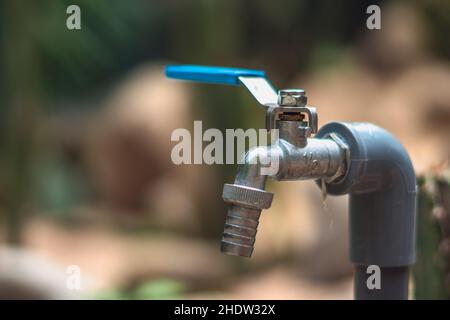 Metal water tap spigot stainless steel faucet lever ball valve blue handle connected to adapter manatee pipe. Blur background. Garden nature work Stock Photo