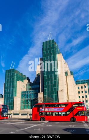 Red double decker buses pass MI6 building at Vauxhall, London UK in December