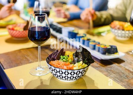 Bowl of fresh Poke and glass of red wine served on a restaurant table with assorted seafood and sushi ready for a party of people to eat Stock Photo