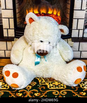 A large beige teddy bear sits near a home fireplace. Stock Photo