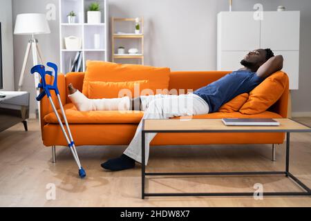 Broken Leg In Cast Recovery. Man With Injury On Sofa Stock Photo