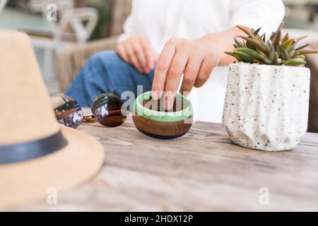 white flowers, bracelet with charm, succulent in pot on the wood table. woman hands. Close up, copy space Stock Photo