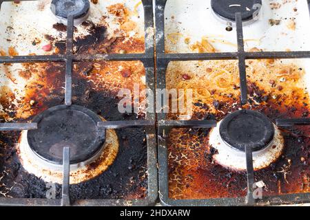 Dirty gas stove surface. Two gas burners and cast iron grate of a gas oven surrounded by old leftovers of food and drinks. Top area surface and burner Stock Photo