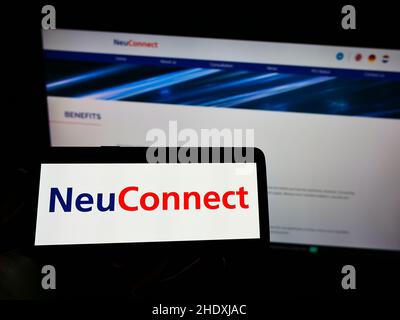 Person holding cellphone with logo of power transmission project NeuConnect Interconnector on screen in front of webpage. Focus on phone display. Stock Photo