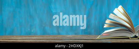Open book, hardback books on wooden table on teal background. Back to school,education,reading. Panoramic, copy space Stock Photo