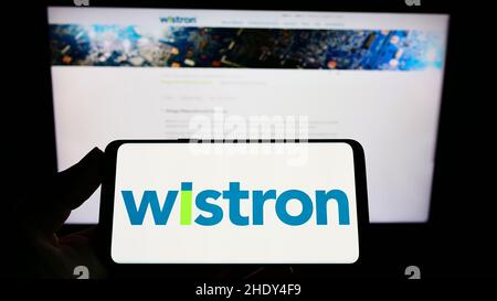 Person holding smartphone with logo of Taiwanese electronic company Wistron Corporation on screen in front of website. Focus on phone display. Stock Photo