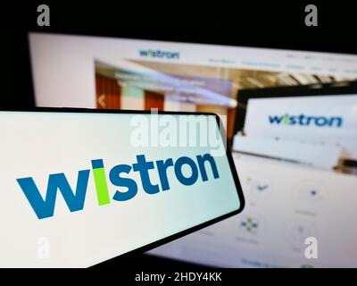 Mobile phone with logo of Taiwanese electronic company Wistron Corporation on screen in front of website. Focus on center-left of phone display. Stock Photo