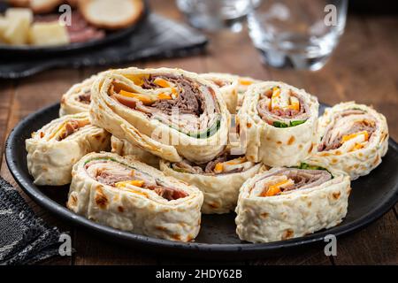 Tortilla wraps made with roast beef, turkey, cheese and lettuce piled on a black plate Stock Photo