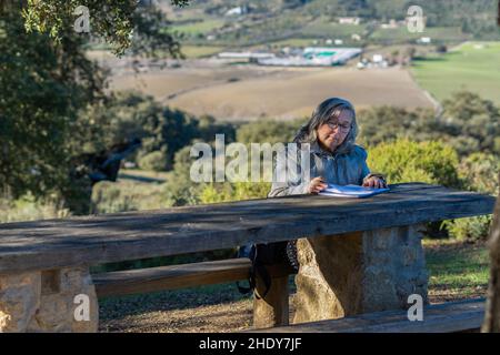 white-haired woman with glasses taking notes in her notebook in the park on a sunny winter's day Stock Photo