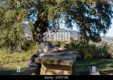 white-haired woman with glasses taking notes in her notebook in the park on a sunny winter's day Stock Photo