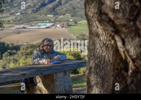 white-haired woman with glasses taking notes in her notebook in the park on a sunny winter's day Stock Photo