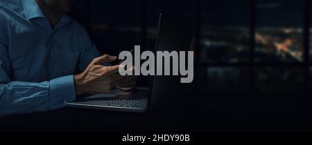 man working in dark office at night. using mobile phone and laptop. copy space Stock Photo