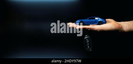hand holding miniature automobile model and key on dark background. car buying and rental. banner Stock Photo