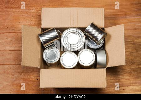 Cans of preserves in a cardboard box on a wooden table in a top view Stock Photo