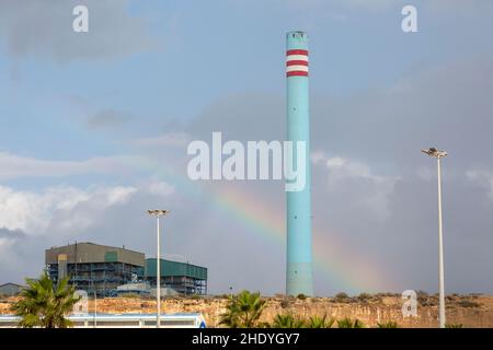 Rainbow in stormy sky behind tall blue industrial cement factory chimney, Carboneras, Almeria, Spain Stock Photo