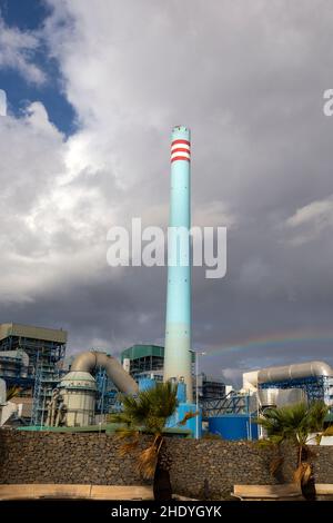 Rainbow in stormy sky behind tall blue industrial cement factory chimney, Carboneras, Almeria, Spain Stock Photo