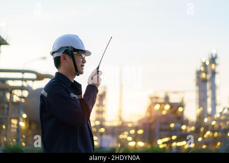 Asian man technician Industrial engineer using walkie-talkie and holding bluprint working in oil refinery for building site survey in civil engineerin Stock Photo