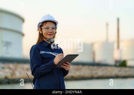 Asian engineer woman are checking the maintenance of the oil refinery factory at evening via digital tablets. Stock Photo