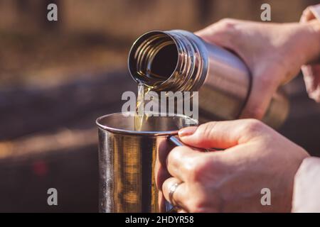 https://l450v.alamy.com/450v/2hdyr58/woman-pours-hot-tea-out-of-thermos-into-metal-cup-in-autumn-forest-refreshment-during-hiking-in-nature-2hdyr58.jpg