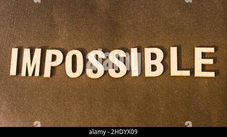 The word Impossible written with Brown Wooden Alphabet stamp on Vintage background. Stock Photo