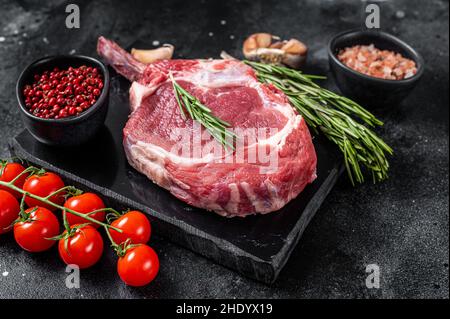 Cooking Raw Rib eye or Tomahawk beef steak with spices. Black background. Top view Stock Photo