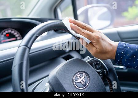 Bangkok, Thailand, July 1, 2021 New Normal, Asian working woman cleaning steering wheel and console in car with white tissue. Stock Photo