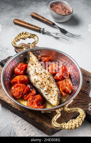 Fried halibut fish steaks with tomato in skillet. White background. Top view Stock Photo