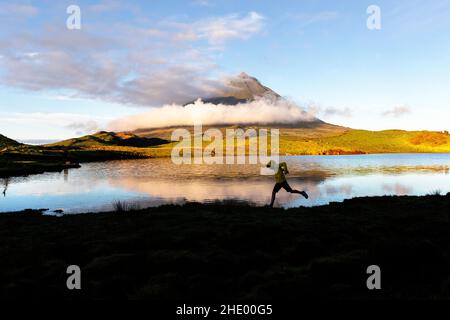 Boy jumping at the lake while first sunlight falling on Ponta da Pico, on Pico Island, Lagoa do Capitão, Azores, Portugal Stock Photo