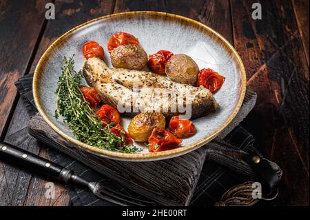 Grilled halibut fish steaks with tomato and potato in plate. Wooden background. Top view Stock Photo
