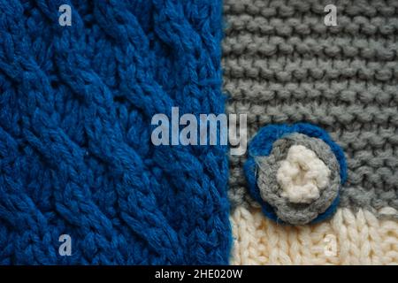 Knitted scarf pattern. Blue and gery threads. Small knitted flower on a scarf. Stock Photo