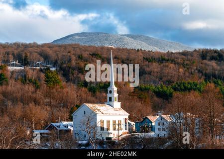 Small village surrounded by pine and maple tree forest with snow covered mountains in background. Stock Photo