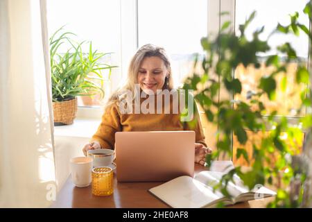 Joyful happy middle-aged woman chatting online on laptop at home, making video call via internet, overjoyed 50s female looking at computer screen spre Stock Photo