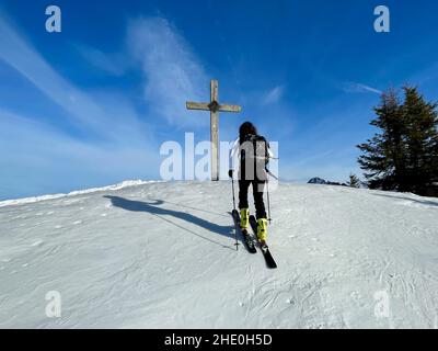 Ski tourer approaching wooden summit cross in Austrian Alps. Laterns, Vorarlberg, Austria. Stock Photo