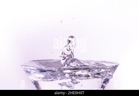 Drop of water falling on filled glass making an isolated splash with a white background Stock Photo