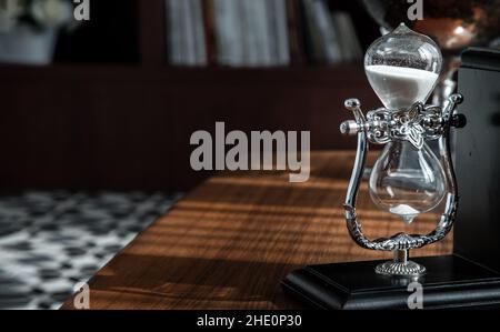 Chiang Rai,Thailand - Sep 06, 2020 : Hourglass on desk with the background of bookshelves in library. Past moments concept with copy space, Selective Stock Photo