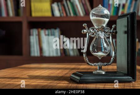 Chiang Rai,Thailand - Sep 06, 2020 : Hourglass on desk with the background of bookshelves in library. Past moments concept with copy space, Selective Stock Photo