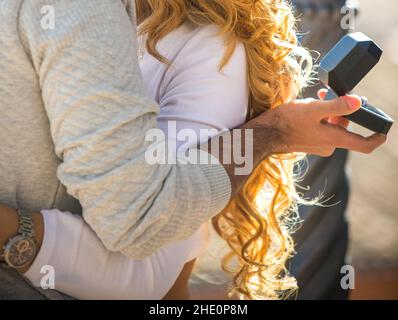 hugging couple. Man holds an open jewellery box with expensive proposal ring. Girl with curly red hair Stock Photo