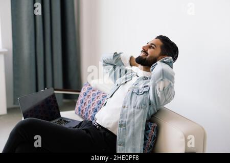 Happy man relaxing on couch while video calling using laptop at home sitting on sofa and making a video call. Stock Photo