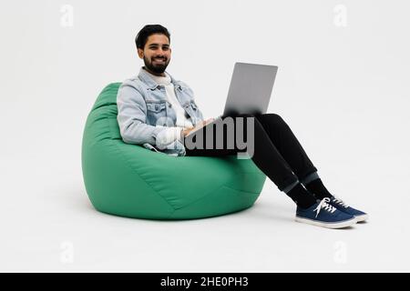 Young man holding notebook browsing chatting colleagues sitting comfy soft armchair wear specs casual denim outfit isolated on white background Stock Photo