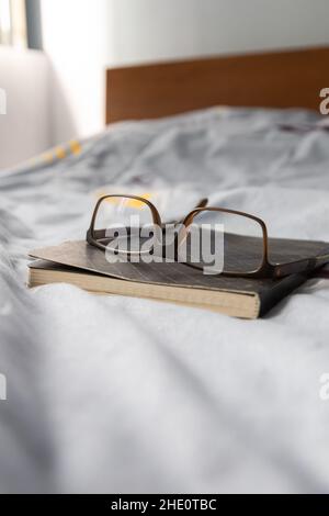 modern glasses on a closed notebook on a bed with light blue background, lifestyle and intellectual pastimes, reading and accessory Stock Photo