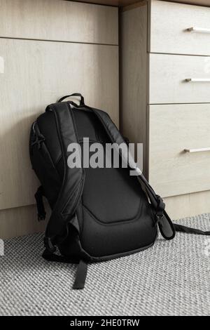 black fabric backpack with straps on a carpet and leaning against a desk, texture detail Stock Photo