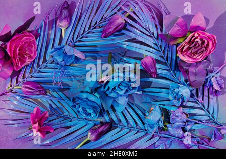 A background or wallpaper made of blue palm tree leaves and pink and purple flowers on violet background. Surreal trendy concept for backdrop or sprin Stock Photo