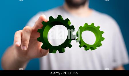 Male's hand holding an illustration of green metallic gears and cogs Stock Photo